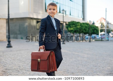 Concept future businessman. Business meeting. Low angle of future businessman in formal wear walking around the street carrying a braun briefcase and holding jacket with arm, urban background.