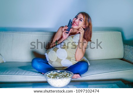young happy hispanic latin woman at home sofa couch watching television eating popcorn relaxed and cheerful enjoying alone TV comedy movie or funny show in girl domestic lifestyle concept