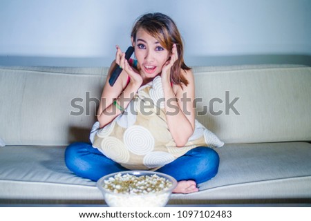 young happy hispanic latin woman at home sofa couch watching television eating popcorn relaxed and cheerful enjoying alone TV comedy movie or funny show in girl domestic lifestyle concept