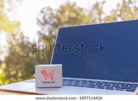 Mini cardboard box and cart icon on laptop keyboard with nature background. Consumers can buy products directly from seller over internet using web browser. Online shopping and e-commerce concept.