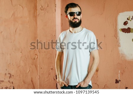 A young stylish man with a beard in a white T-shirt and glasses. Street photo