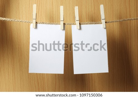 Blank paper hangs on the brown rope with Wooden paper clips on wood background for design in your work concept.