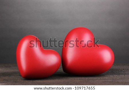 Two decorative red hearts on wooden table on grey background