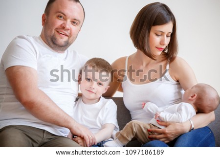 Image of happy married couple with two young sons sitting on sofa
