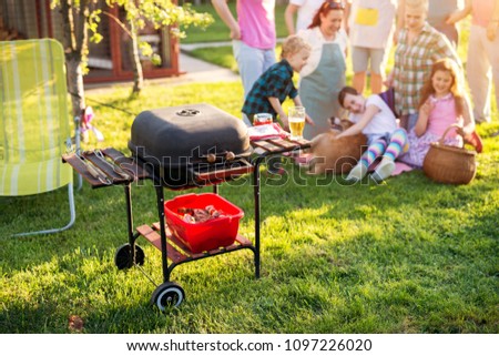 Picture of old vintage in good shape grill in a yard with a family playing with a dog in the background.