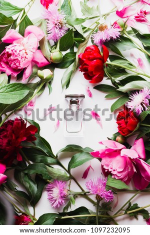 Pink bottle of women's perfume next to the flowers of peony. Spring gentle fragrance for women. Top view, flat lay