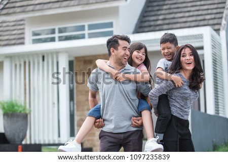 two kids with their parent having fun together in front of their new house. piggyback ride Royalty-Free Stock Photo #1097235839