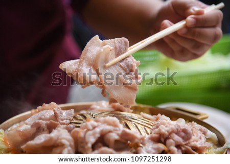 Hand hold the chopsticks with Bacon,Thai Barbecue buffet,called Moo Kra Ta. Royalty-Free Stock Photo #1097251298
