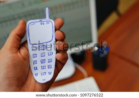 Made of paper a mobile phone with an antenna in a man's hand on the background of a desktop in the office