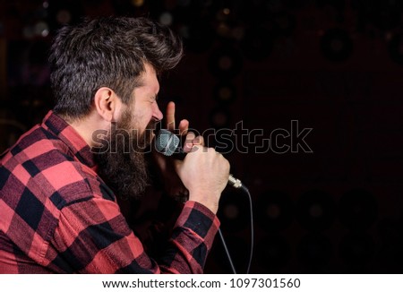 Talented vocalist concept. Man on tense face holds microphone, singing song, black background, copy space. Musician, vocalist with beard and mustache lighted by spotlight