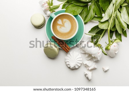 A cup of coffee on a white table with peonies, sweets and fruits