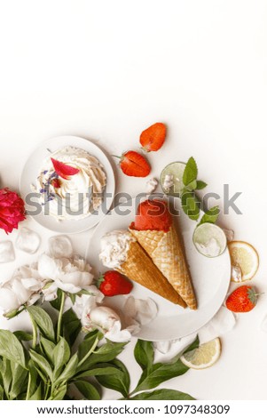 Strawberry and cream ice cream on a white plate on a table with white peonies, slices of lime, lemon, fresh strawberries and cakes.