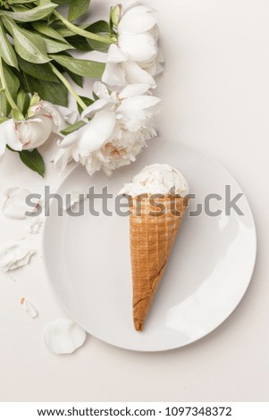 Flatlay of sweet cones of cream ice cream on a white plate and white peonies on a white background, top view, copy space