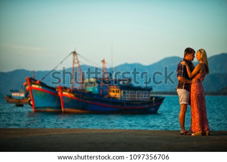 young couple standing on the background of the sea and ships at sunset