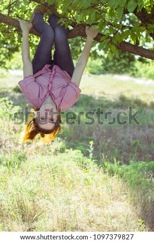 Cheerful girl hanging on a tree upside down Royalty-Free Stock Photo #1097379827
