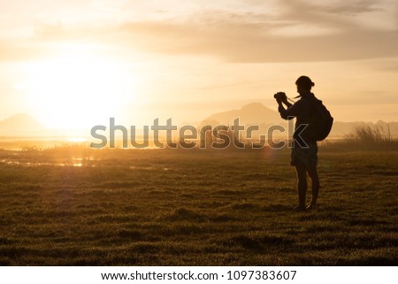 silhouette of a woman holding a smartphone taking pictures outside during sunrise or sunset. Travelling and vacation concept.