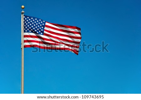 US American flag waving in the wind with beautiful blue sky in background