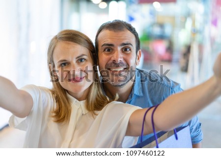Smiling middle-aged couple taking selfie photo in mall