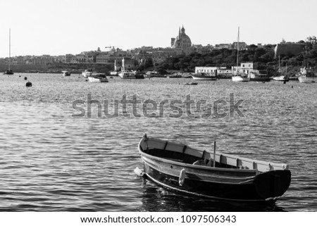 Cityscape view with Basilica of Our Lady of Mount Carmel on the island of Malta. Yachts docked at the port of Valletta. A shabby old boat among the luxury ships. Black and white picture