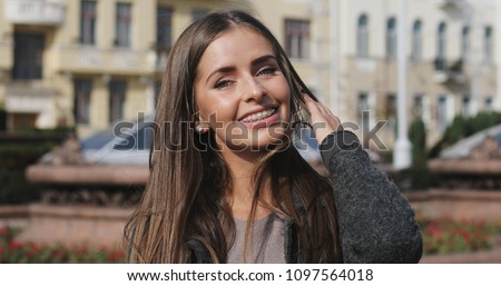 Young girl with braces on teeth looking at camera and smiling. Happy long hair brunette woman in the center of city. Sunny day. 