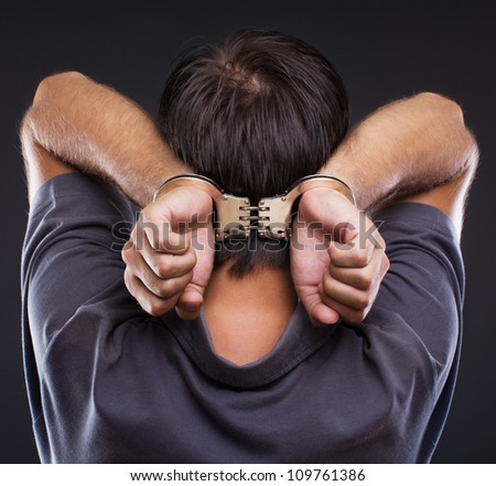 Man in handcuffs with hands on neck on gray background