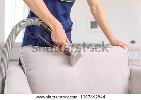 Dry cleaning worker removing dirt from armchair indoors Royalty-Free Stock Photo #1097662844