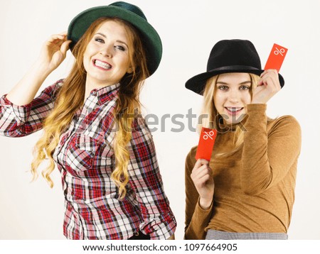 Female friends on shopping showing tag with sale percentage sign enjoying cheap clothing.