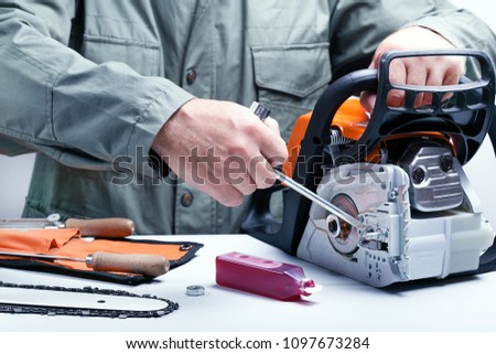 Repair of chainsaws,gasoline powered tools. Man repairing chainsaw. Royalty-Free Stock Photo #1097673284