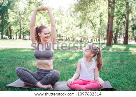 Nice picture of mother and daughter sitting on one carimate. They are sitting in lotus position. Woman is stratching and keeping her hands up. Small girl is looking at mom with wonder. Yoga and