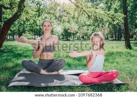 A picture of woman is sitting on the back with her daughter sitting in the front. They are sitting in lotus position and stratching their left hands. Yoga and Pilates Concept