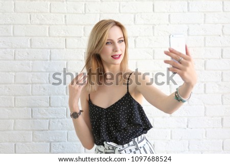 Attractive young woman taking selfie near brick wall