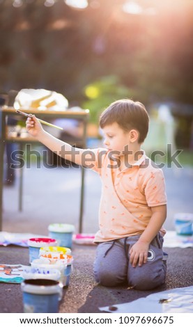 Cute kid near the park painting his picture with watercolors into the park