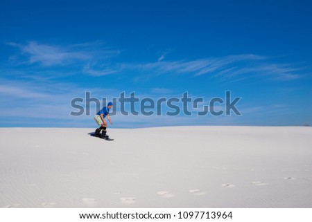 Sand boarding in desert at sunny day. Man trains to snowboard on sand dunes against of blue sky. Wide angle.