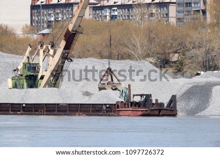 port cranes unload crushed stone on a barge