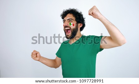 Sport fan screaming for the triumph of his team. Man with the flag of Mexico  makeup on his face and green t-shirt.
       