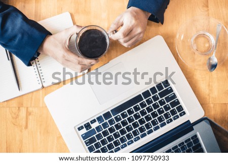 Top view of one businessman hands holding a cup of black coffee near his laptop computer, good for work life or business theme background