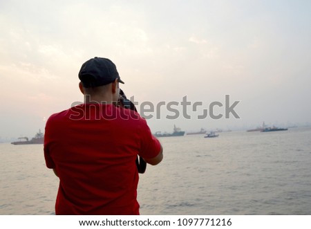 A photographer taking photo in holiday place Elephanta caves in Mumbai India. He is standing in boat in the mid of sea water way of Island Elephanta cave and taking photograph of ocean and sea gulls.
