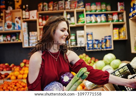 Girl in red holding different vegetables on fruits store.