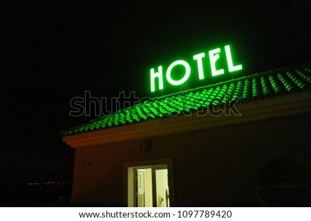 Hotel signal placed on the roof illuminated at night, luminous green neon