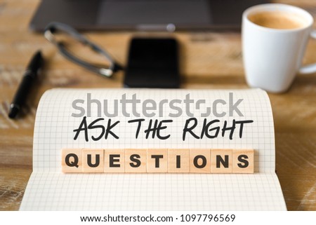 Closeup on notebook over wood table background, focus on wooden blocks with letters making ASK THE RIGHT QUESTIONS text. Concept image with laptop, glasses, pen and mobile phone in background