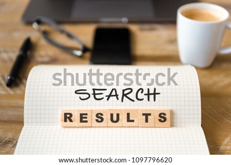 Closeup on notebook over wood table background, focus on wooden blocks with letters making SEARCH RESULTS text. Business concept image. Laptop, glasses, pen and mobile phone in defocused background