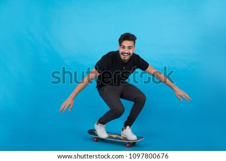 Full-length shot of young man standing on the skateboard spread his arms balancing himself on a blue background.