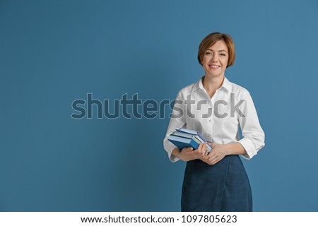 Portrait of female teacher with notebooks on color background