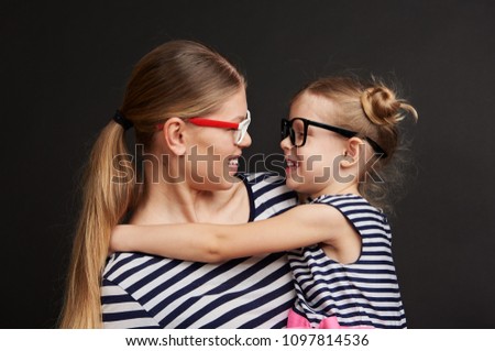 Portrait of joyful child hugging her mom wearing glasses. Studio portrait of mother and daughter looking at each other. 