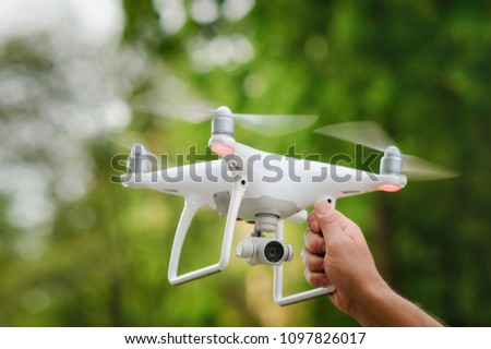 Man holding with his hand white quadcopter over green trees background. Operation of drone in air