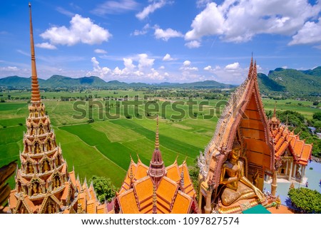 Aerial view of Tiger Cave Temple ( Wat Tham Suea) with the green rice field and blue sky background at Kanchanaburi province, Thailand