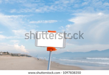 Selfie photo concept : Mock up Extensible selfie stick or monopod with mobile phone taking picture shot at sea beach and blue sky view outdoor background.