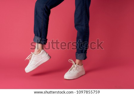legs in blue pants and sneakers on a pink background                           