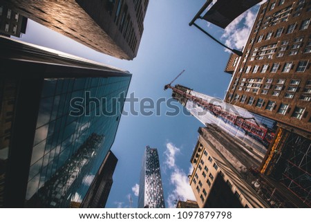 Ultra-wide angle picture of New York City sky scrapers in Downtown Manhattan taken during morning rush hour with the sun shining through the building's alleyway. 