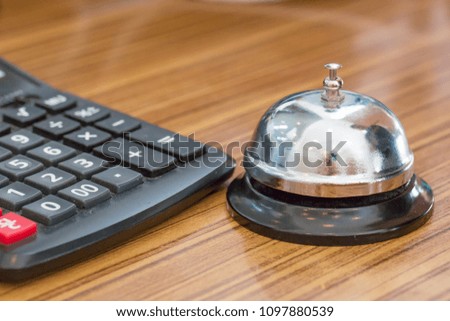 Service bell and calculator. There are on wooden table in a restaurant.
